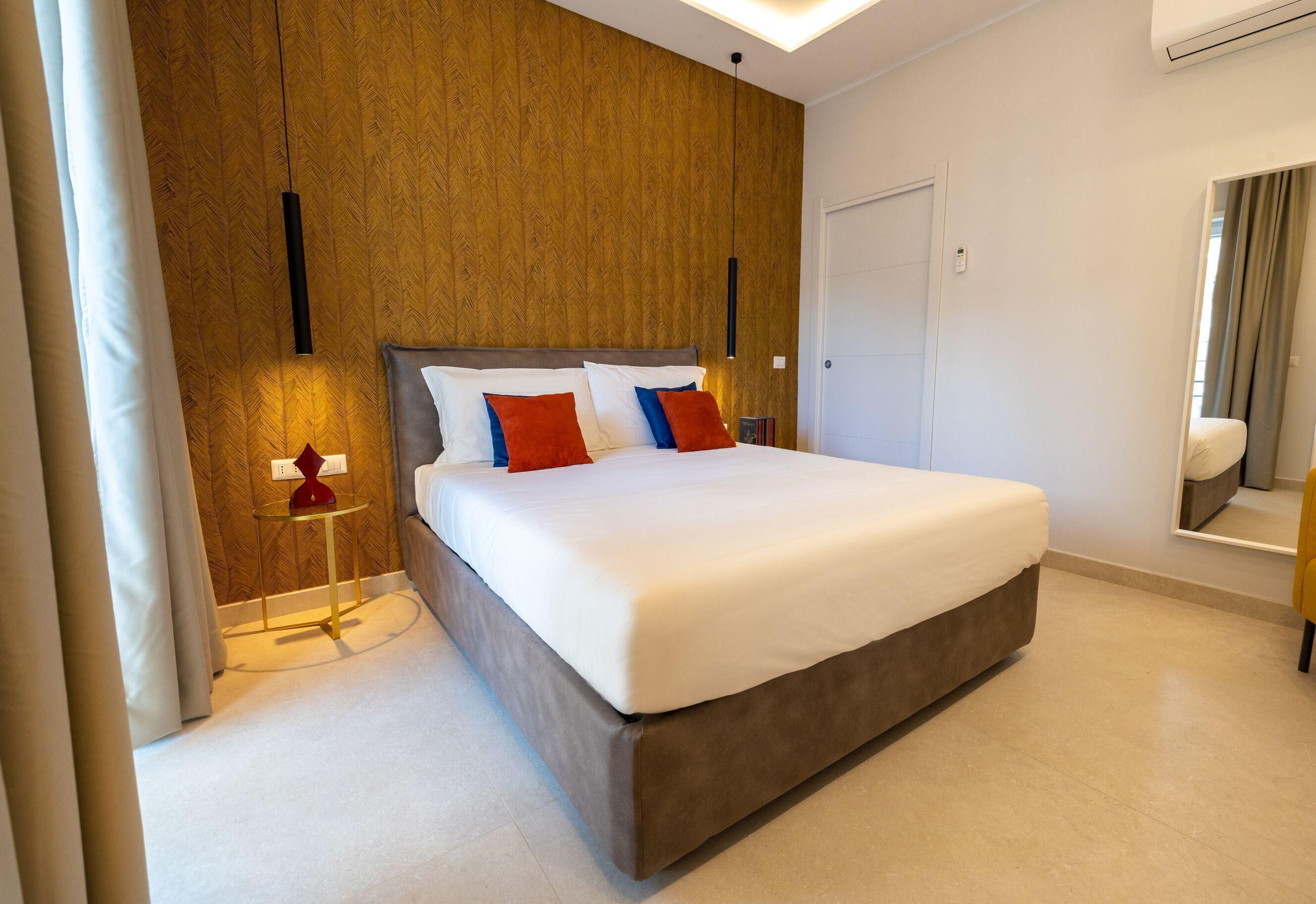 A modern bedroom with a large bed, wooden panel walls, a small bedside table, and a mirror.