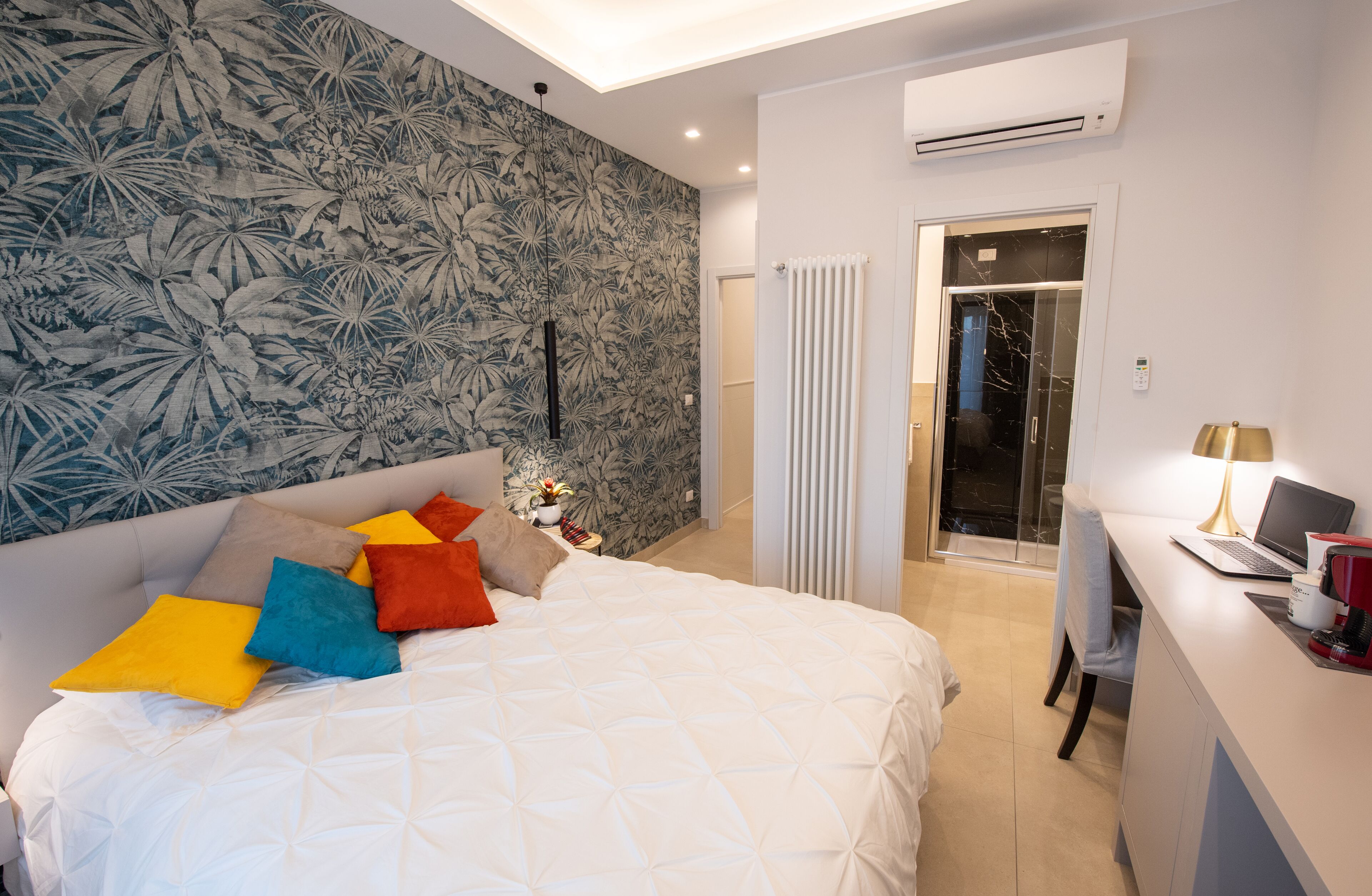 A modern hotel room with a large bed, a desk with a laptop, and a shower area.