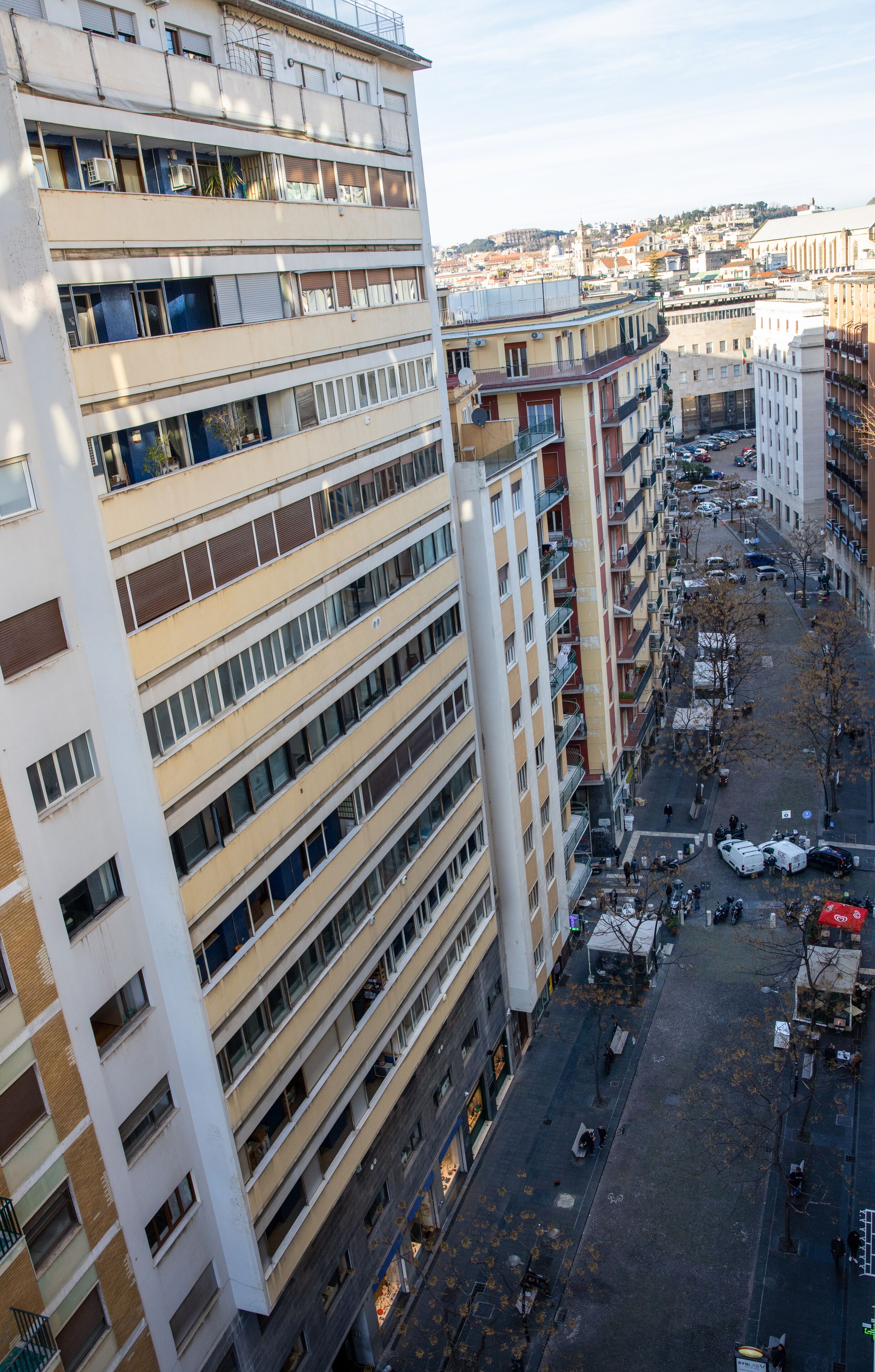 A multi-story building with balconies, a street in front, and parked cars.