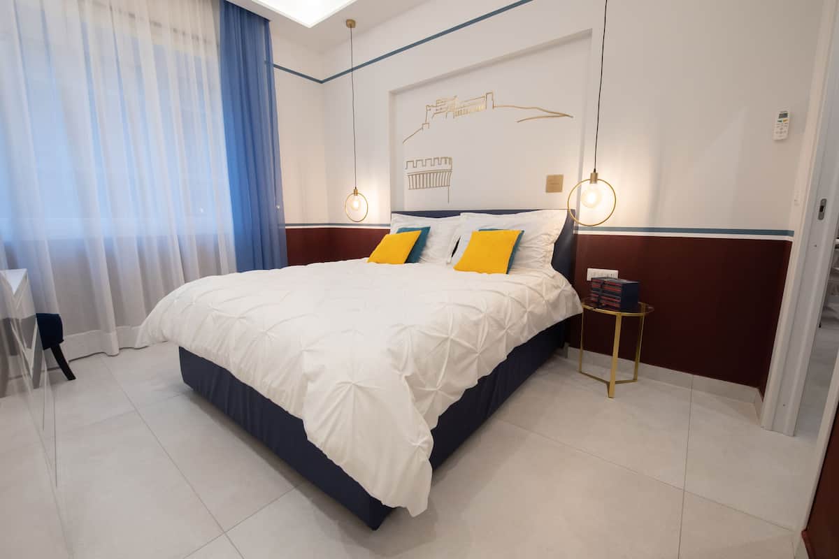 A modern hotel room with a large bed, a bedside table, and a view of the cityscape through the window.