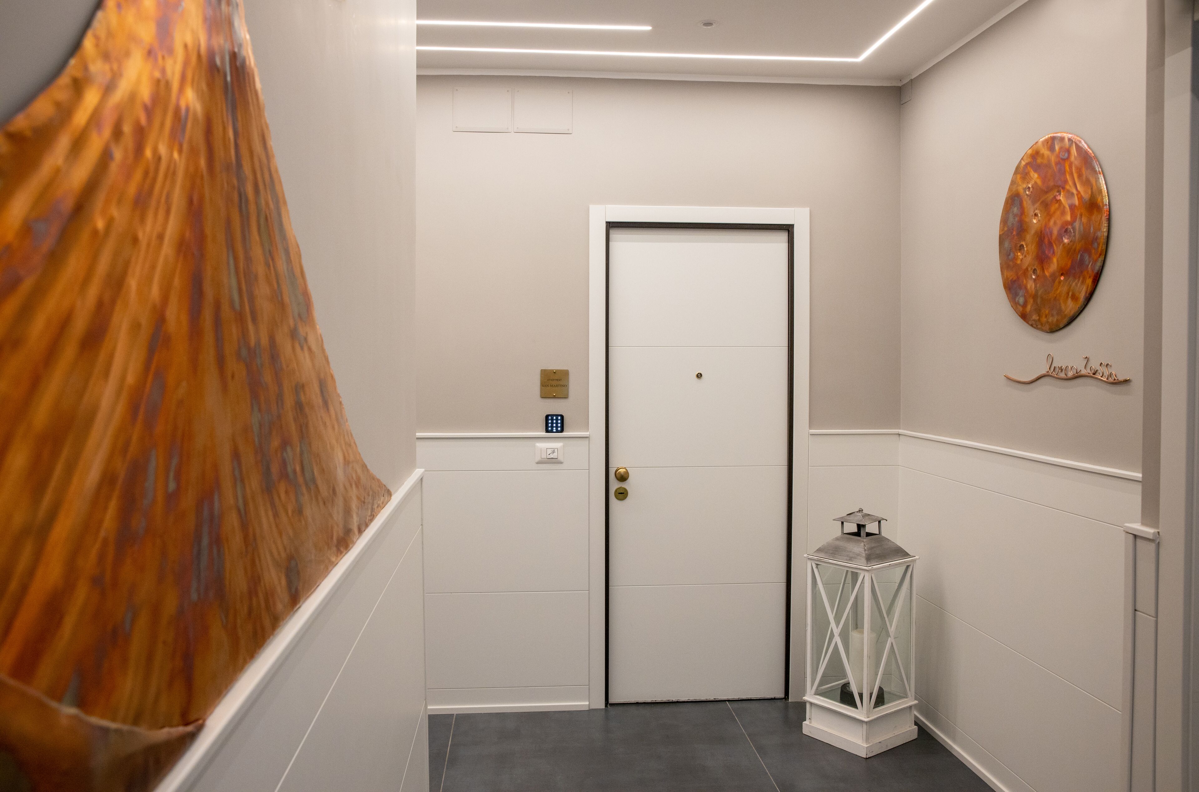 A hallway with a white door, a wall-mounted circular artwork, and a small white lantern.