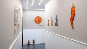Un couloir agrémenté d’installations d’art moderne, un mur blanc orné d’une œuvre circulaire et deux petites figurines en bois à l’extrémité.