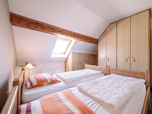 A bedroom with two beds, wooden wardrobe, skylight, and a bedside lamp.