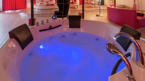 Un área de spa moderna con un amplio jacuzzi iluminado rodeado de sillas negras.