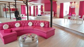 Una habitación de hotel moderna con un sofá seccional rosa, una mesa de centro redonda y un espejo grande.