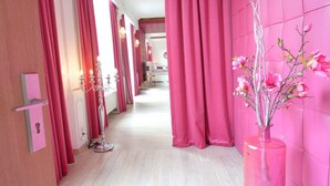 Un pasillo con cortinas rosadas, un jarrón con flores rosas y un candelabro.