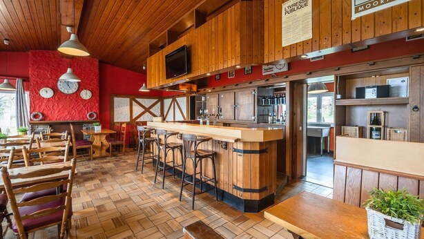 A rustic bar area with wooden furniture, a bar counter, and a television mounted on the wall.