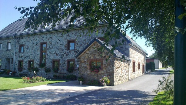 Un bâtiment en pierre avec un toit en pente, un petit porche agrémenté de jardinières et une allée pavée.