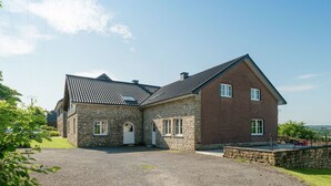 A two-story stone house with a sloped roof, a gravel driveway, and a fenced yard. - Spacious Holiday Home in Chodes with Sauna (Malmédy-Boussire)