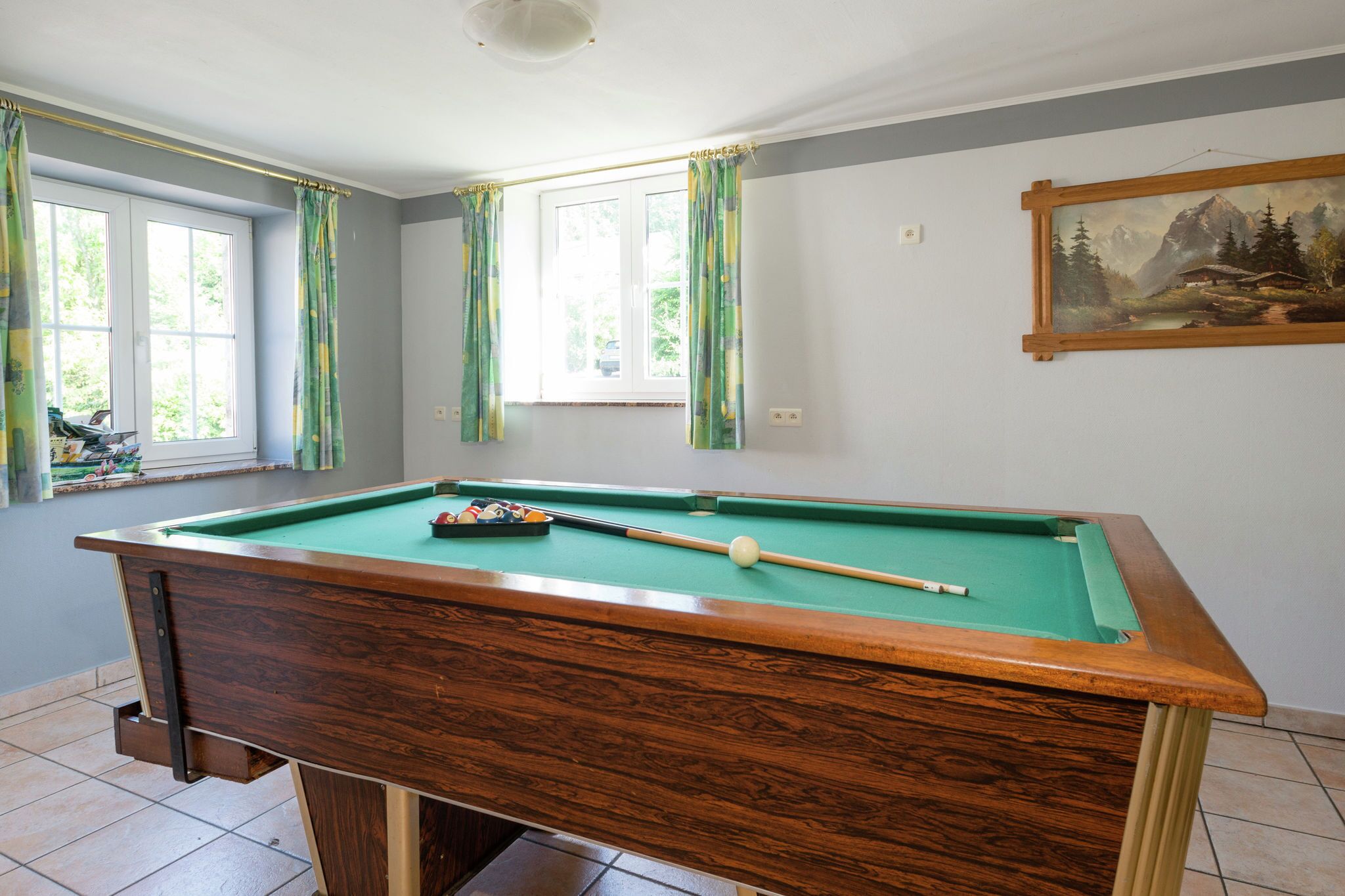 A pool table in a room with two windows, a painting on the wall, and a door.