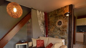 A cozy living room with a sofa, a small table with a bowl of fruit, a lamp, and a stone wall.