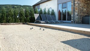 A modern building with a stone facade, a covered patio with lounge chairs, and a view of a forested hillside. - Holiday Home in Stoumont with Private Pool (Stoumont)