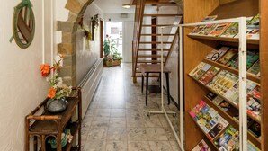 A hallway with a stone archway, a wooden staircase, and a bookshelf filled with magazines.