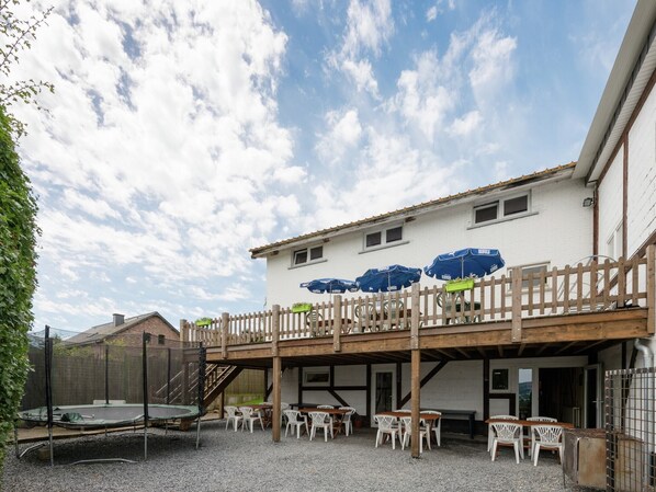 Un espacio al aire libre cubierto con mesas y sillas, un trampolín y una terraza de madera.