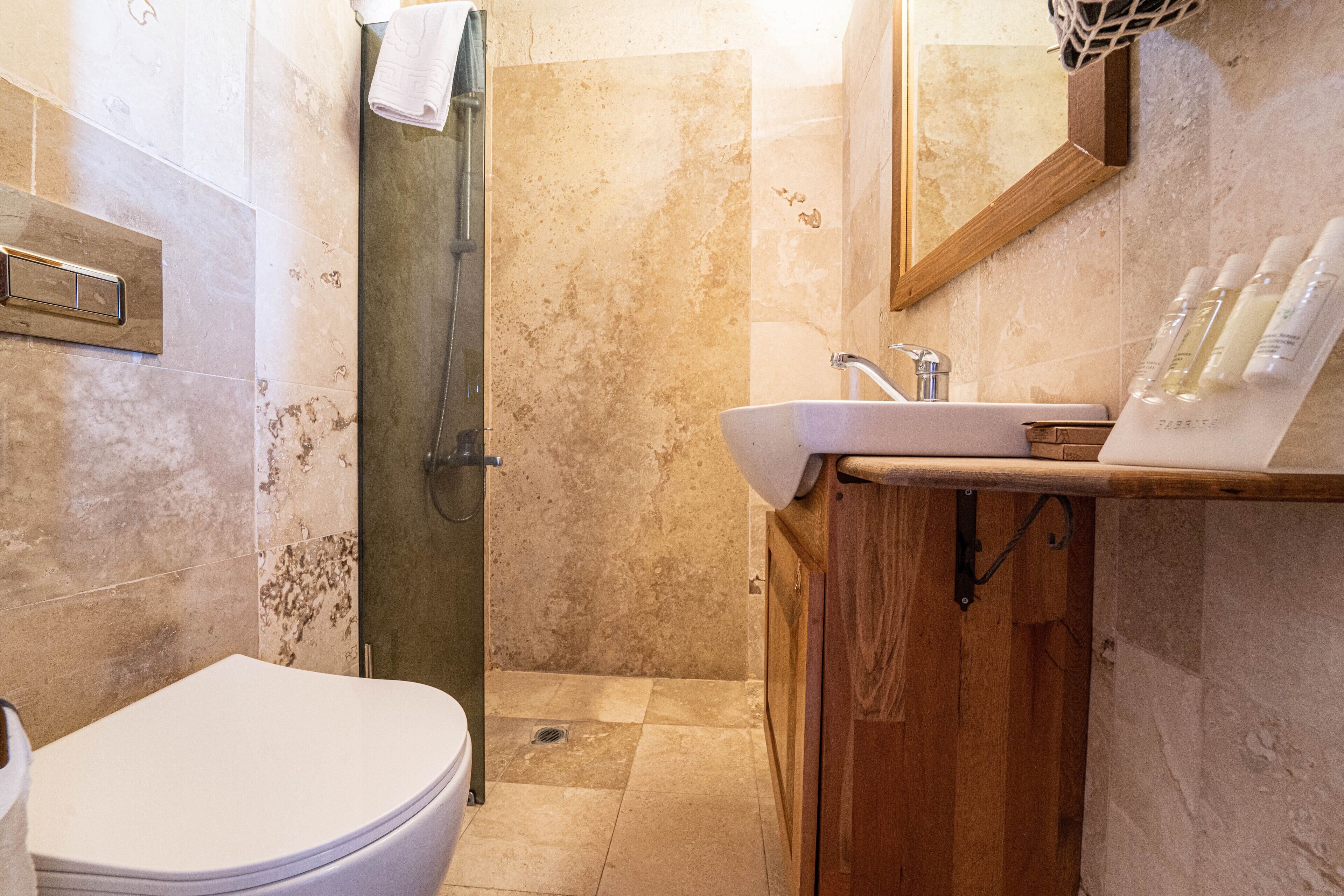 A bathroom with a toilet, shower, sink, and wooden cabinet.