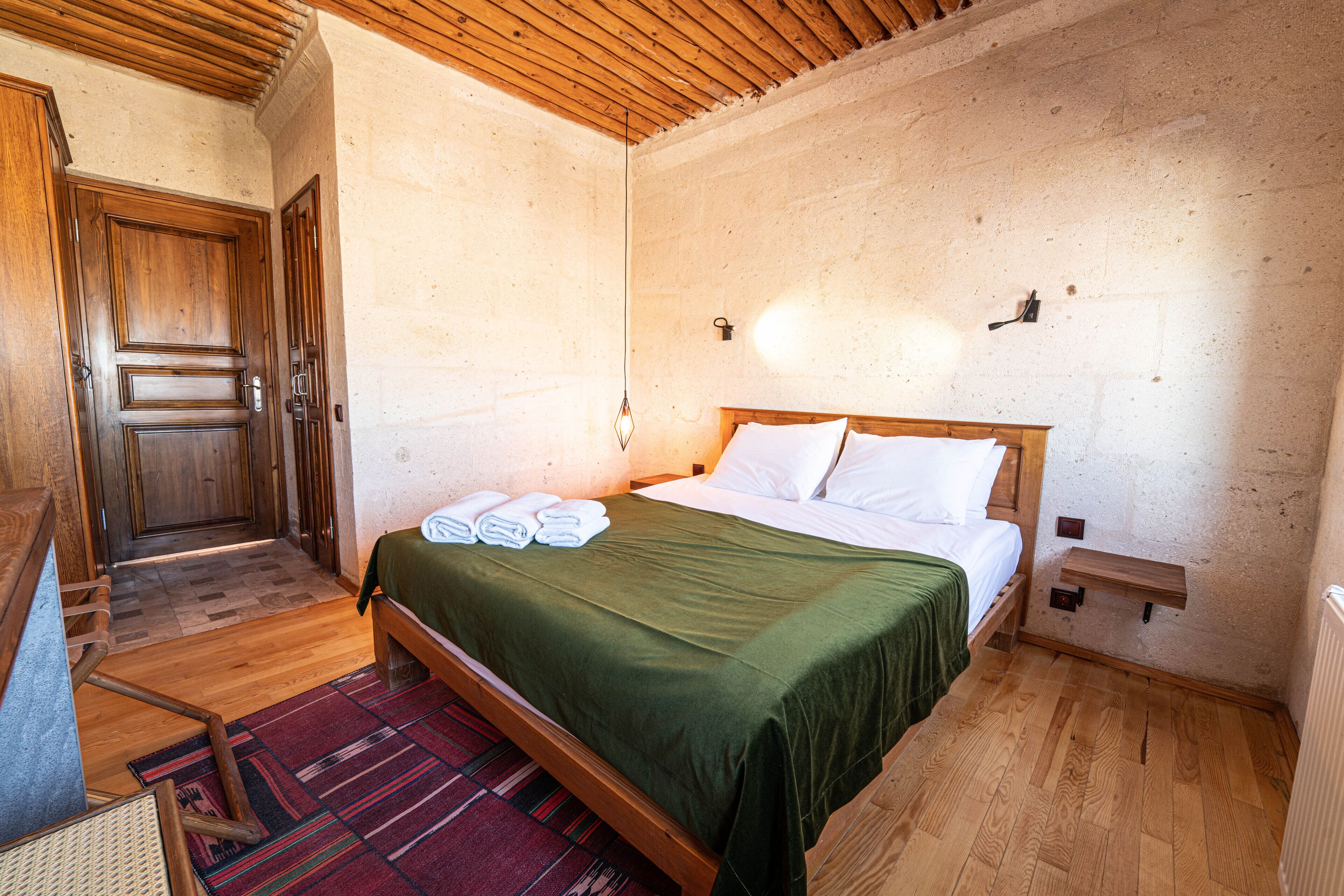 A bedroom with a wooden bed, a green bedspread, and a wooden floor.