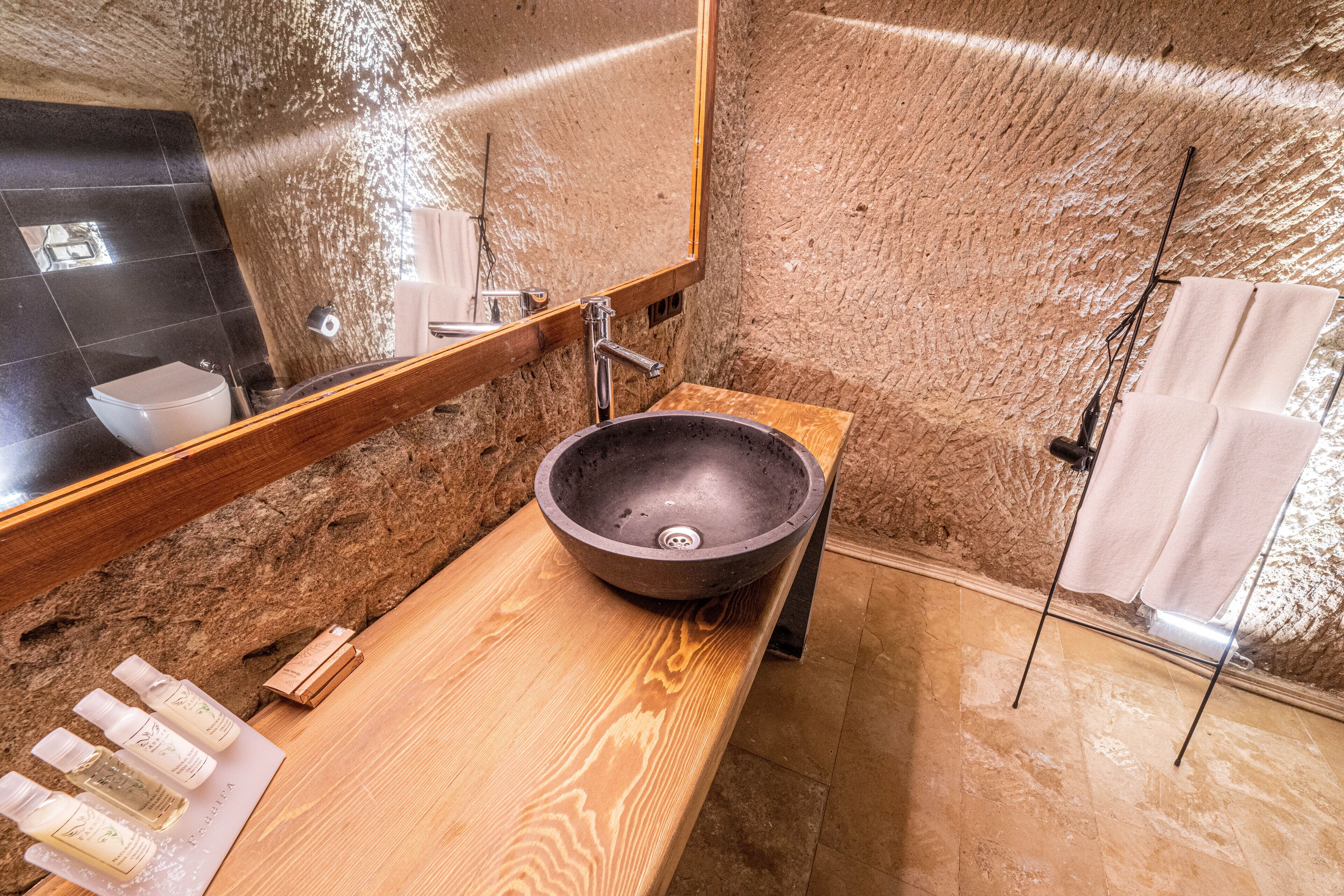 A bathroom with a wooden vanity, a large mirror, a black basin, and a shower area.