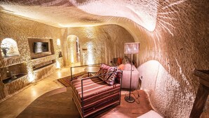 A cozy, cave-like bedroom with a bed, a TV, and a lamp. - Alice in Cappadocia (Nevsehir)