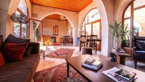 A spacious living area with a wooden ceiling, arched windows, and a central coffee table with books. - Alice in Cappadocia (Nevsehir)