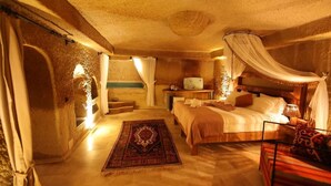 A cozy bedroom with a canopy bed, a bedside table with a lamp, and a decorative rug. - Alice in Cappadocia (Nevsehir)