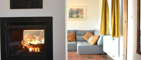 A living room with a fireplace, a sofa with cushions, and a window with curtains.