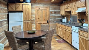 A rustic kitchen with wooden cabinets, a dining table with wicker chairs, and a refrigerator.