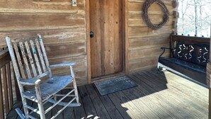A wooden cabin with a porch, a wooden door, a bench, and a chair.