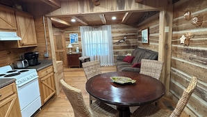 A cozy cabin-style kitchen with wooden cabinets, a dining table with wicker chairs, a stove, and a coffee maker.