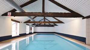 Una piscina interior con suelo de baldosas, vigas de madera y paredes blancas.