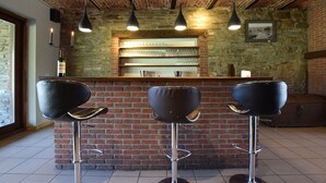 Una zona de bar con tres taburetes negros, una pared de ladrillo y lámparas colgantes.