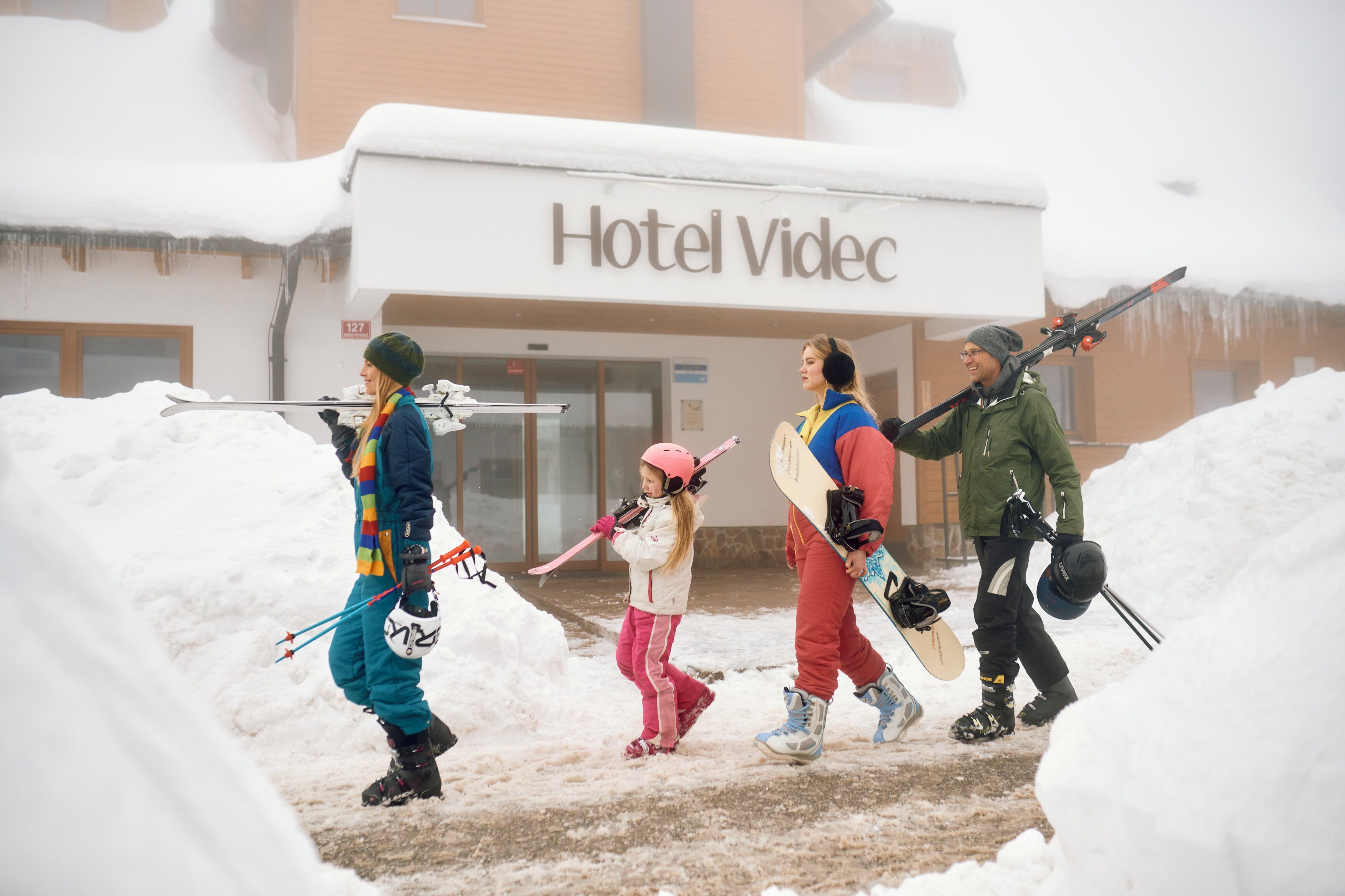 Un grupo de personas con esquíes y tablas de snowboard frente a un edificio que dice 