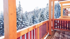 En træterrasse med gelænder, der kigger ud over en sneklædt skov.