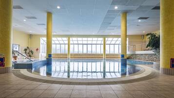 An indoor swimming pool with clear glass walls, yellow pillars, and a tiled floor.