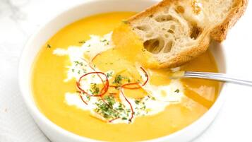 Un tazón de sopa cremosa decorado con hierbas y un trozo de pan.