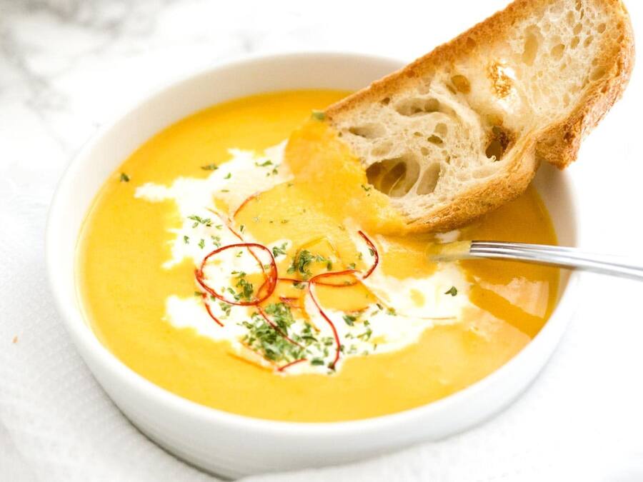 Un bol de soupe crémeuse, garnie d’herbes aromatiques, accompagné d’une tranche de pain.