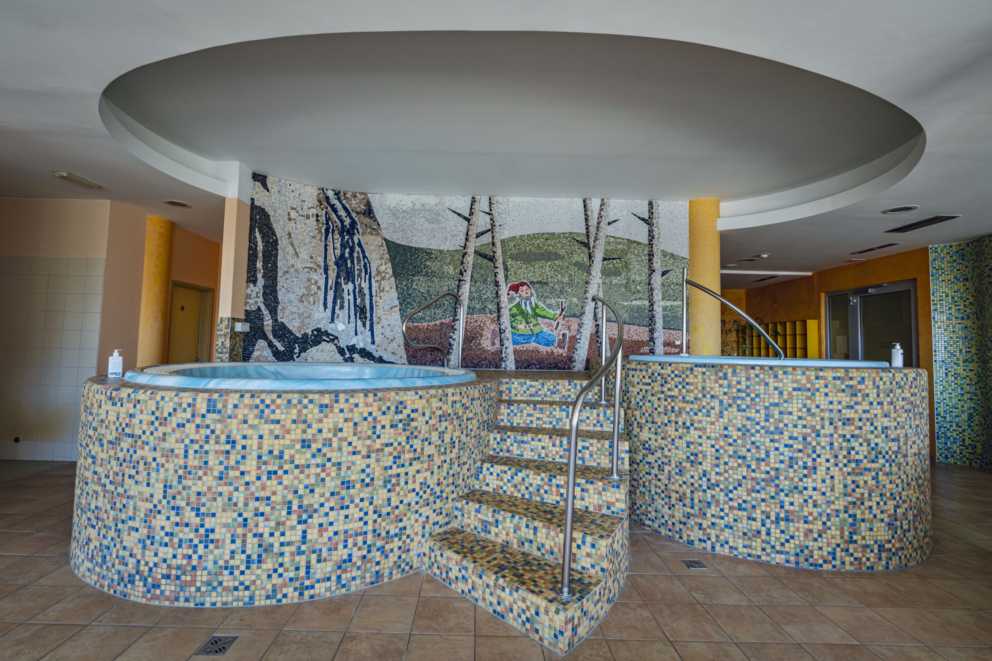 Un espace spa doté de bains à remous aux motifs de mosaïques et d’une fresque représentant une cascade.
