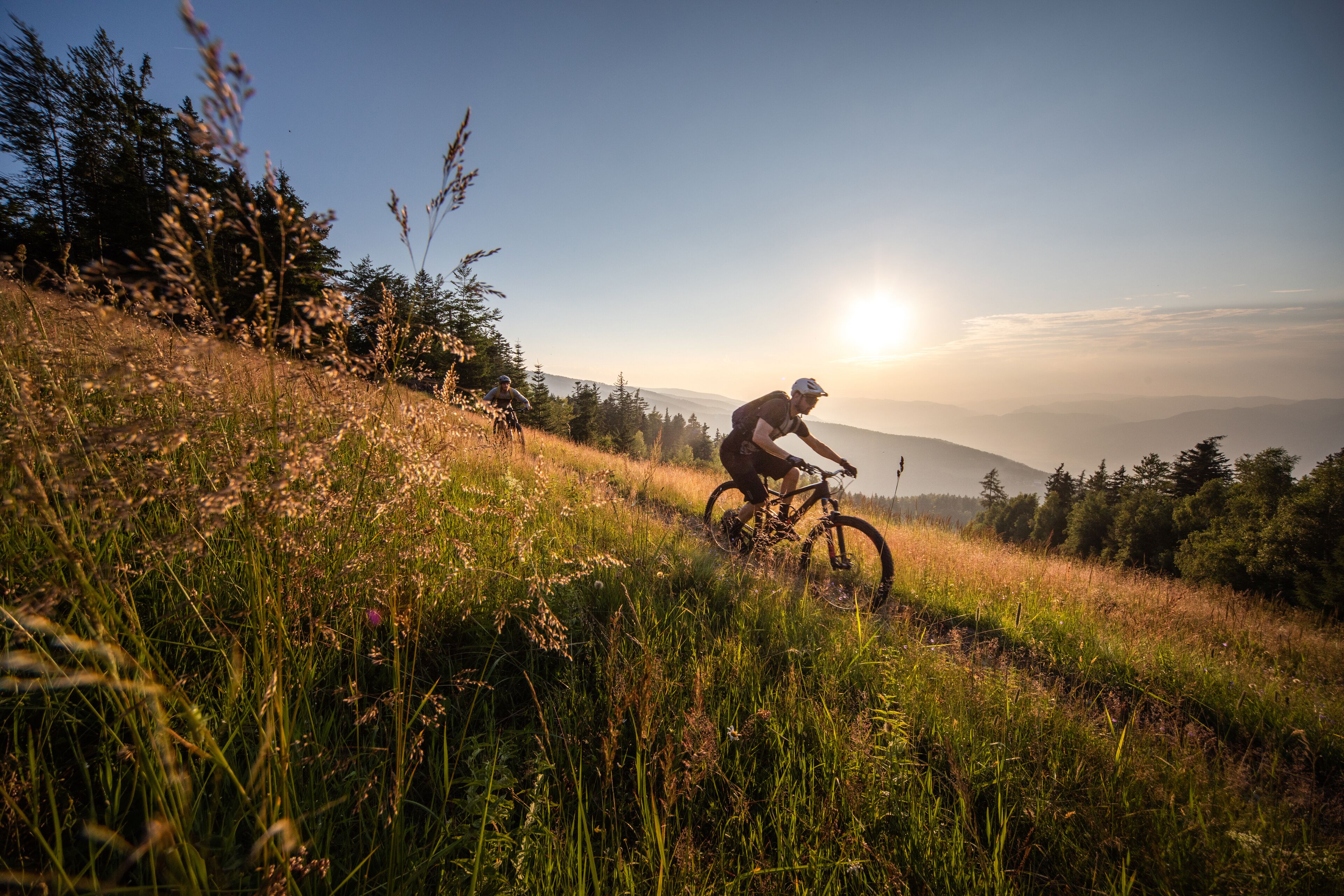 A mountain biker on a trail with a clear sky and distant mountains.