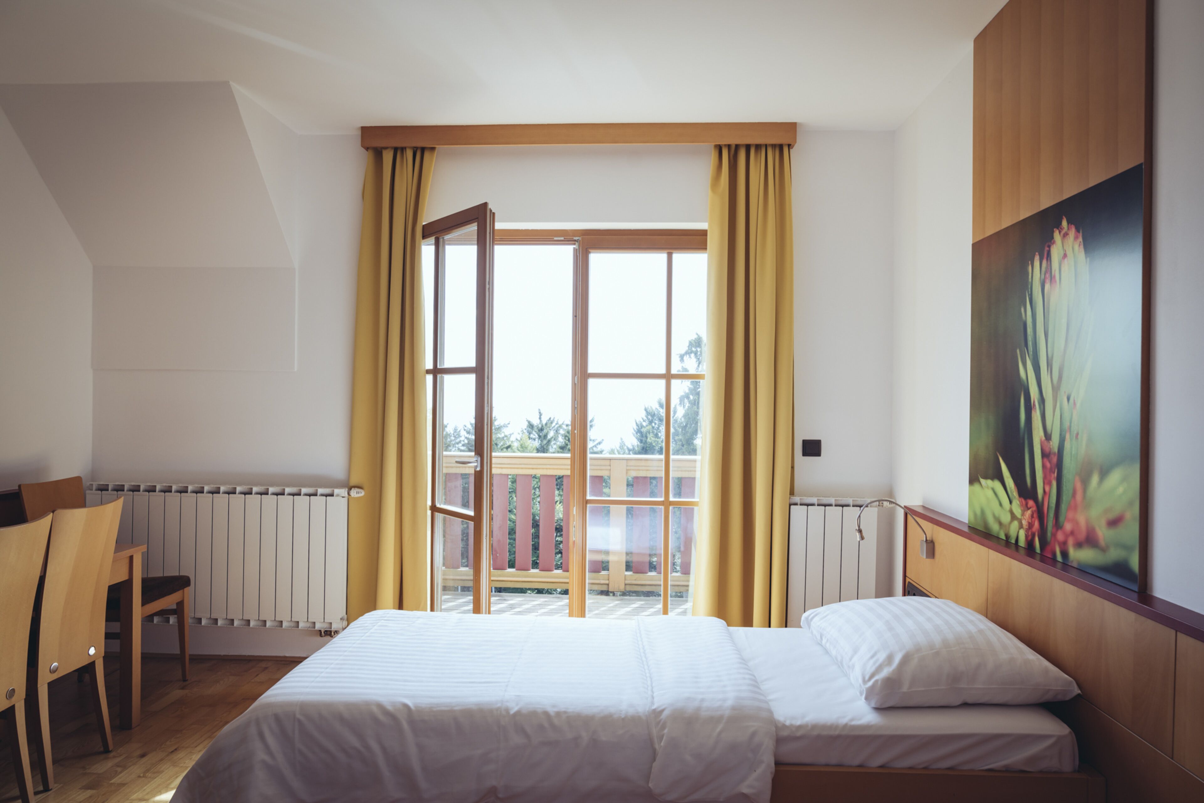 Een slaapkamer met een bed, een stoel, een raam met gordijnen en een schilderij aan de muur.