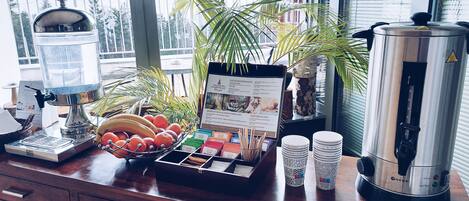 Una zona de bar con una máquina de café, un frutero, un tablero de menú y una pila de platos.
