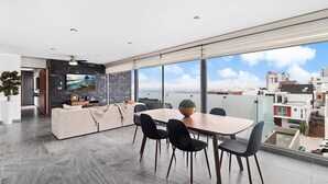 A modern living room with a dining area, large windows, and a city view.