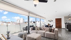 A modern living room with a large sectional sofa, a dining table, and a kitchen area visible through a sliding glass door.