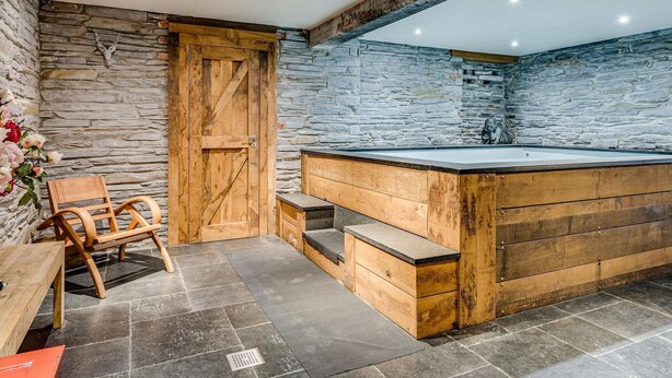 Un baño rústico con pared de piedra, bañera de madera y un banco de madera.