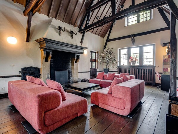 A spacious living room with a fireplace, wooden beams, and large windows. - Group Stay with Spa in Vielsalm (Vielsalm)