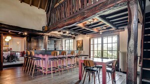 Un interior rústico con vigas de madera a la vista, una zona de bar con taburetes y un comedor con mesa y sillas.
