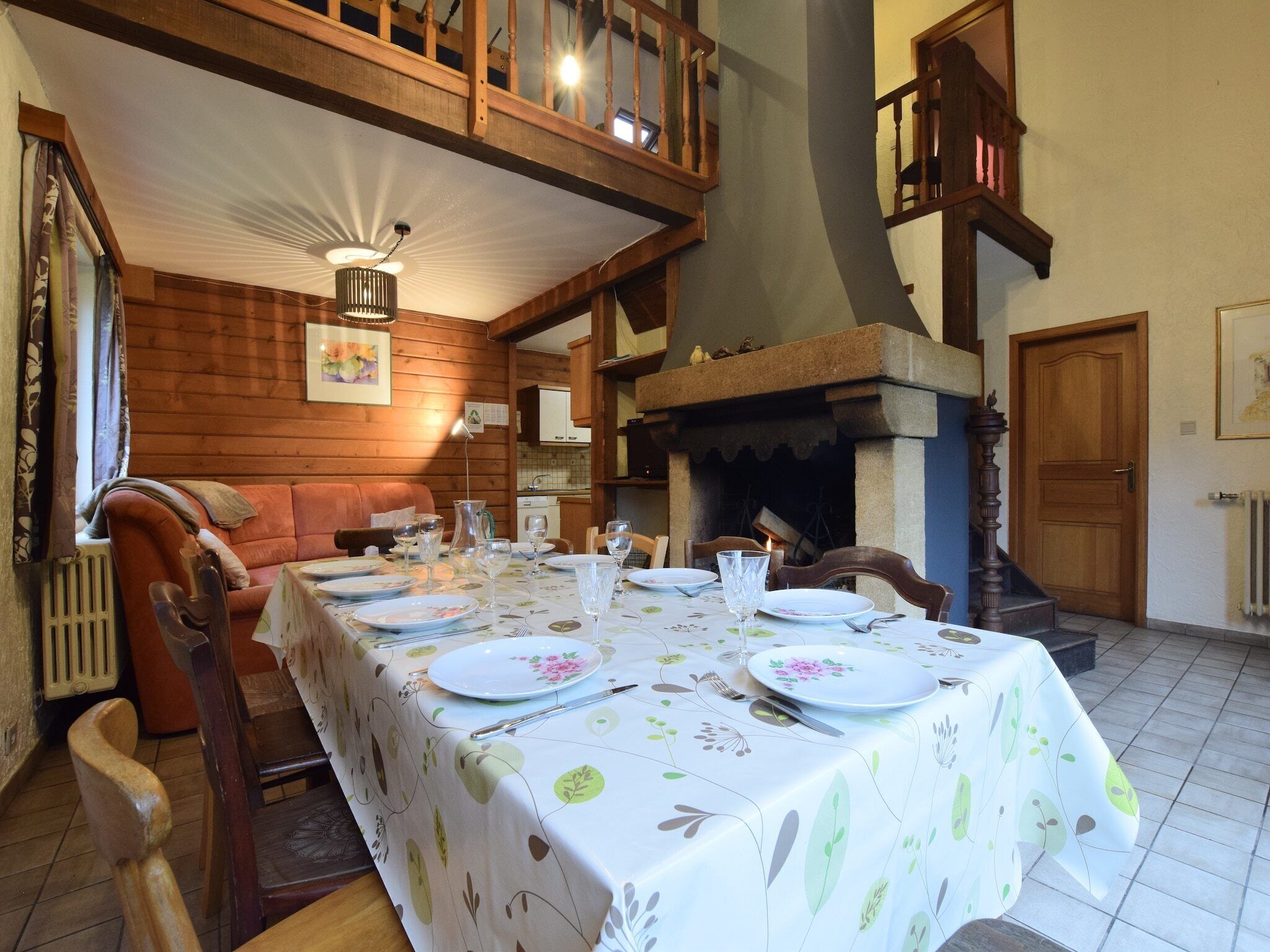 Un comedor con una mesa larga dispuesta para una comida, paredes de madera, una chimenea y una escalera.