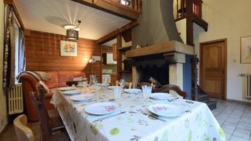Un comedor con una mesa larga dispuesta para una comida, paredes de madera, una chimenea y una escalera.