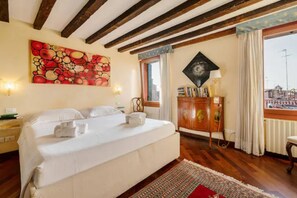 A hotel room with a large bed, wooden beams on the ceiling, a painting on the wall, a window with curtains, and a view of the city. - Rooftop Terrace Penthouse & 360° Views - Venice5th (Venezia)