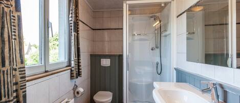 Un baño con ducha, inodoro, lavamanos y ventana con cortinas.