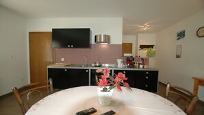 A dining area with a table, chairs, a vase with flowers, and two remote controls on the table.