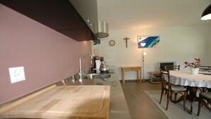 A kitchen with a wooden cutting board, stainless steel sink, and a dining area with a table and chairs.